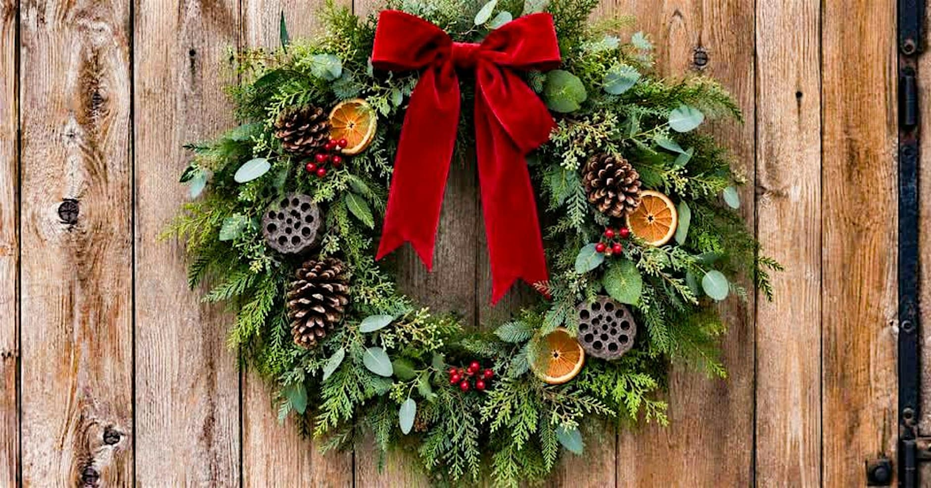 A finished Christmas wreath of fresh evergreen foliage with a red velvet bow, pine cones, dried orange slices and red berries